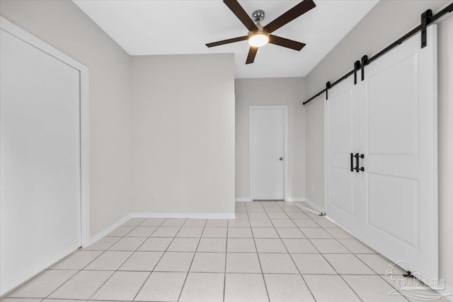 spare room featuring a ceiling fan, light tile patterned floors, baseboards, and a barn door