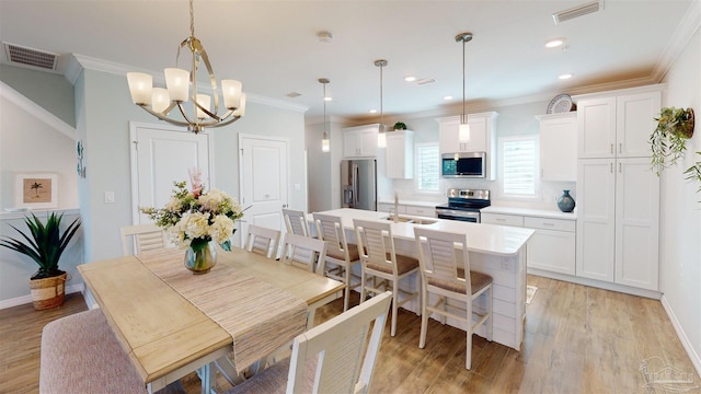 dining room with crown molding, an inviting chandelier, sink, and light hardwood / wood-style flooring