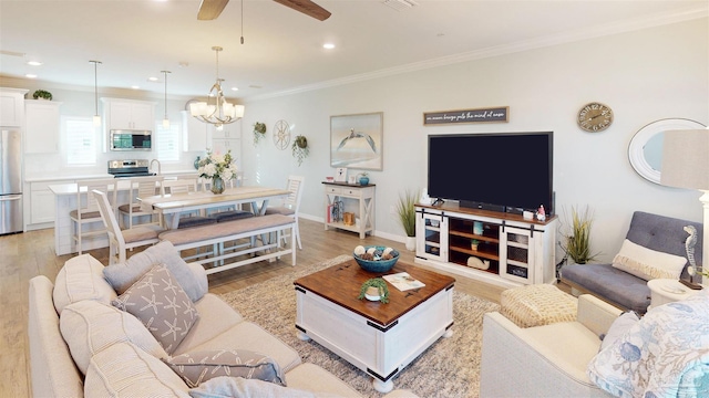 living room with ornamental molding, ceiling fan with notable chandelier, and light wood-type flooring