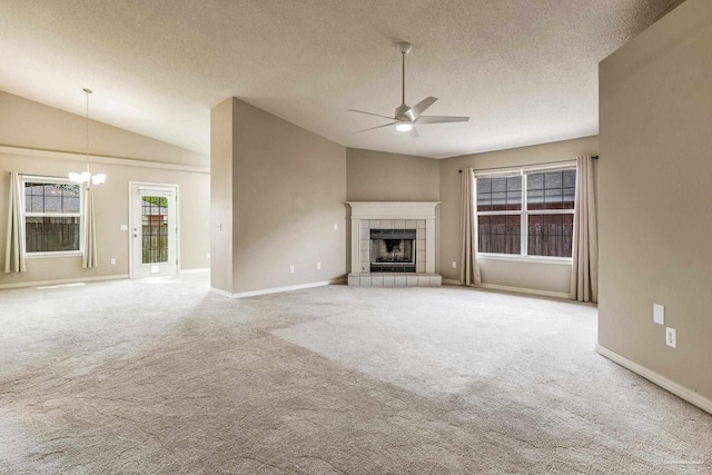 unfurnished living room with ceiling fan with notable chandelier, vaulted ceiling, a tiled fireplace, and light colored carpet