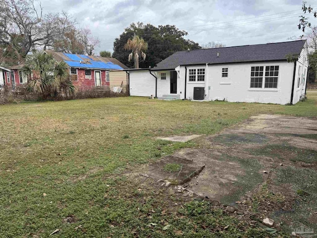 rear view of property featuring central AC, a lawn, and solar panels