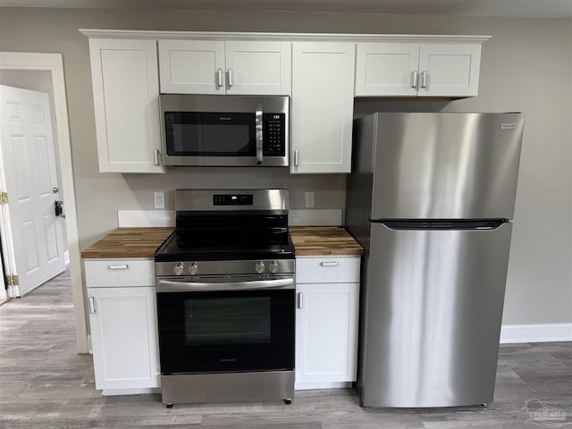 kitchen featuring white cabinetry, appliances with stainless steel finishes, light hardwood / wood-style floors, and wooden counters