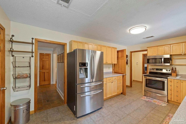 kitchen with appliances with stainless steel finishes, light brown cabinets, and a textured ceiling