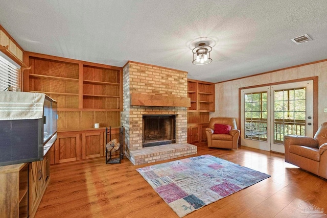 living room featuring ornamental molding, light hardwood / wood-style flooring, a brick fireplace, and a textured ceiling