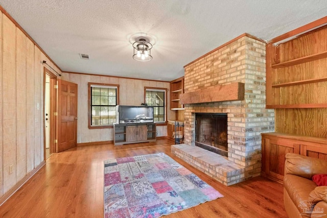 living room with a brick fireplace, a textured ceiling, light wood-type flooring, and built in shelves