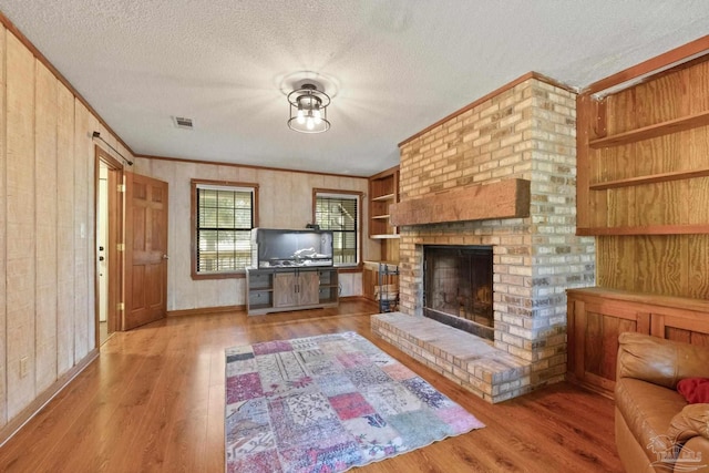 living room with ornamental molding, a textured ceiling, wood finished floors, and visible vents