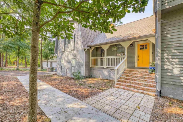 doorway to property featuring a porch and roof with shingles