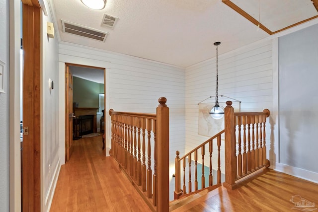 corridor featuring wooden walls, a textured ceiling, and light hardwood / wood-style floors