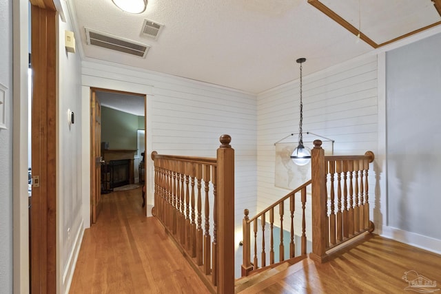 corridor with an upstairs landing, visible vents, wood walls, and wood finished floors