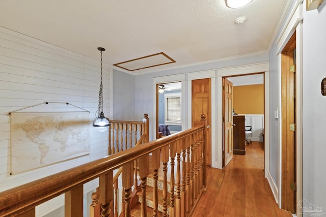 hallway featuring attic access, an upstairs landing, light wood finished floors, a textured ceiling, and crown molding