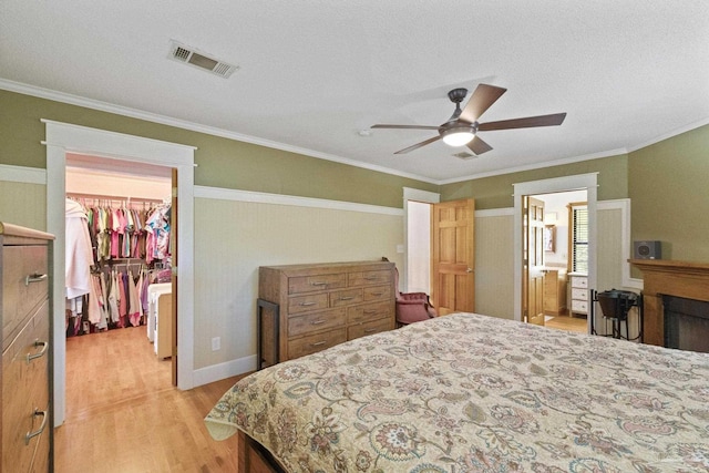 bedroom with crown molding, visible vents, a closet, light wood-type flooring, and a walk in closet