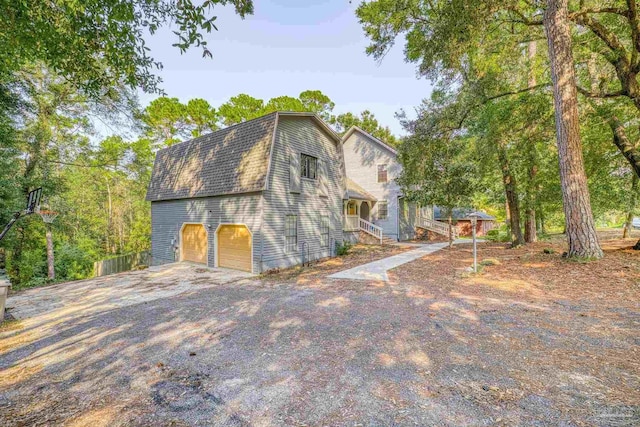 view of front of home with a gambrel roof, a shingled roof, an attached garage, and driveway