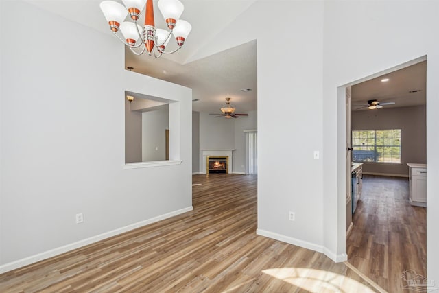 spare room featuring ceiling fan with notable chandelier, light wood-type flooring, and vaulted ceiling