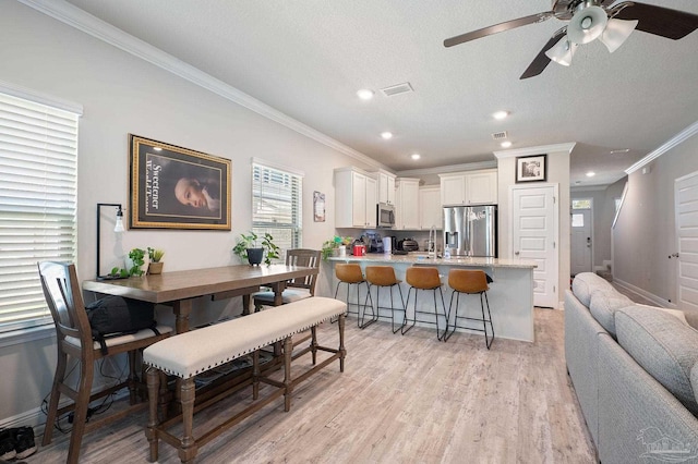 kitchen featuring a kitchen bar, light wood-type flooring, stainless steel appliances, crown molding, and white cabinetry