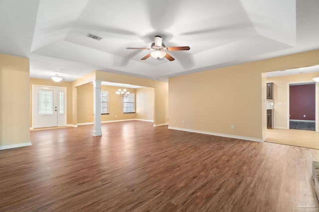 unfurnished living room with decorative columns, a tray ceiling, ceiling fan with notable chandelier, and dark hardwood / wood-style flooring