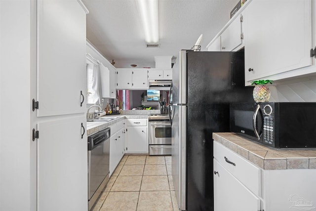 kitchen featuring sink, light tile patterned floors, tile counters, stainless steel appliances, and white cabinets