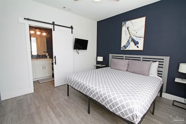 bedroom with ensuite bathroom, sink, light hardwood / wood-style flooring, ceiling fan, and a barn door