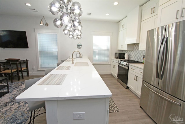 kitchen with white cabinets, appliances with stainless steel finishes, light hardwood / wood-style flooring, and hanging light fixtures