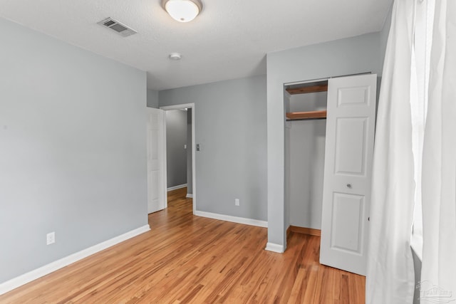 unfurnished bedroom with a textured ceiling, visible vents, baseboards, light wood-style floors, and a closet