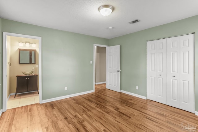 unfurnished bedroom with a closet, visible vents, light wood-style flooring, and baseboards