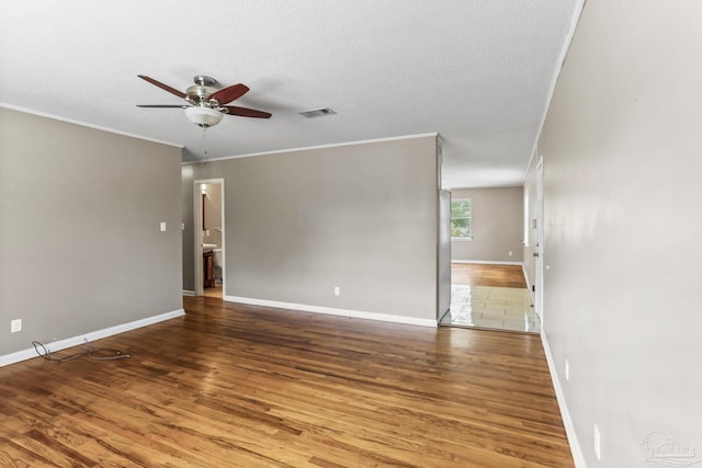 empty room featuring a textured ceiling, wood finished floors, visible vents, a ceiling fan, and ornamental molding