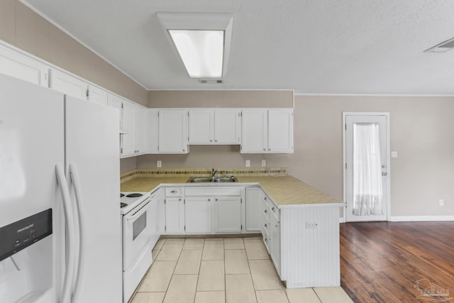 kitchen featuring white appliances, white cabinets, a peninsula, light countertops, and a sink