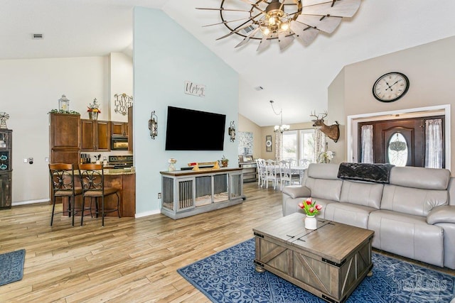 living room with ceiling fan, high vaulted ceiling, light wood-type flooring, a chandelier, and baseboards