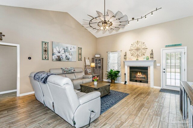 living room with light wood-type flooring, a fireplace, baseboards, and high vaulted ceiling