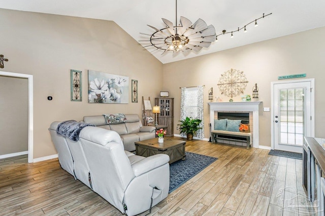 living room featuring light wood-type flooring, a fireplace, baseboards, and high vaulted ceiling