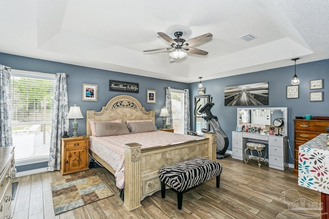 bedroom featuring a raised ceiling, wood finished floors, baseboards, and a ceiling fan