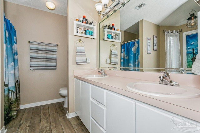 bathroom with a textured ceiling, wood finished floors, toilet, baseboards, and double vanity