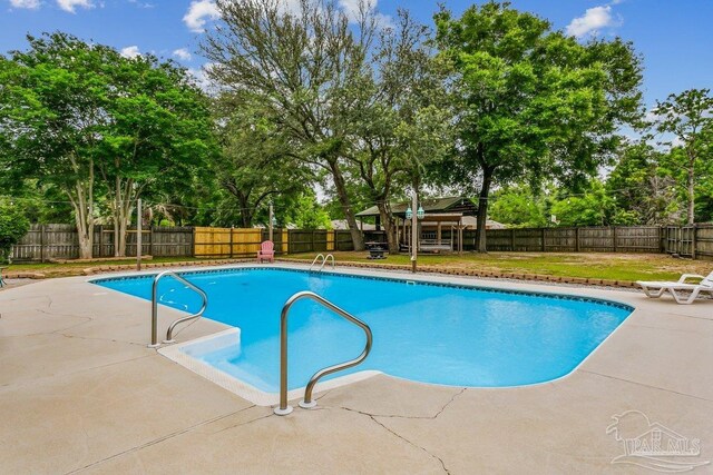 view of pool featuring a patio area, view of wooded area, a fenced backyard, and a gazebo