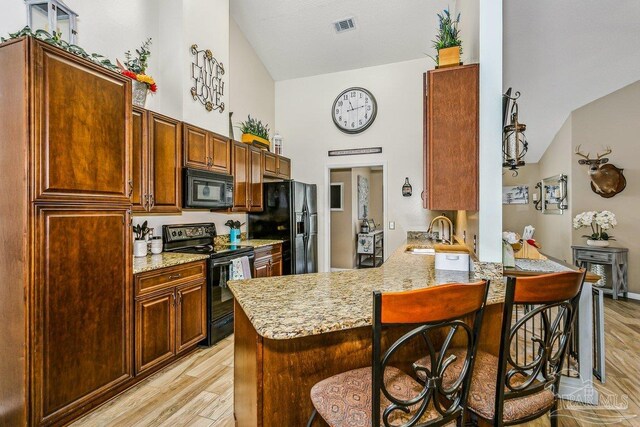 kitchen with black appliances, a sink, a breakfast bar, light wood-style flooring, and high vaulted ceiling