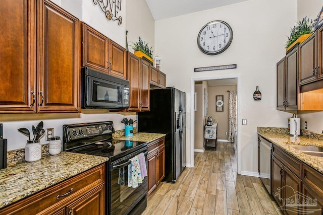 kitchen with black appliances, light stone countertops, light wood-type flooring, baseboards, and a sink