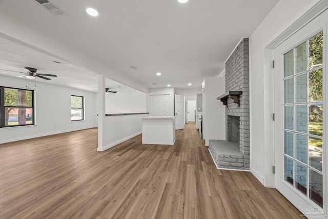 unfurnished living room featuring wood finished floors, a ceiling fan, visible vents, baseboards, and a brick fireplace