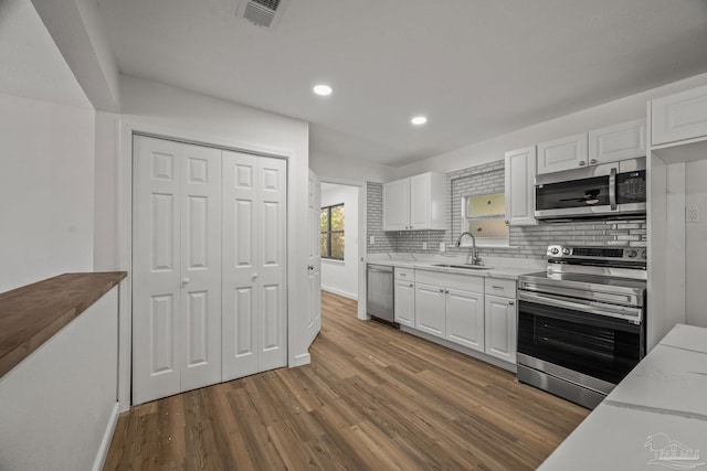 kitchen with wood finished floors, appliances with stainless steel finishes, a sink, and white cabinetry