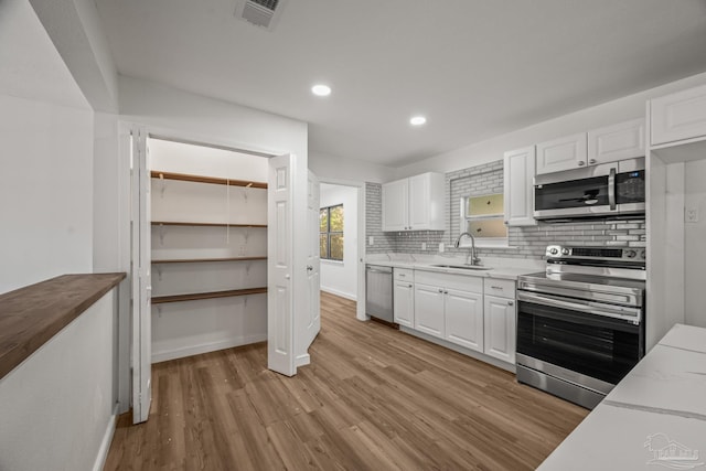 kitchen featuring stainless steel appliances, light wood-type flooring, white cabinets, and a sink