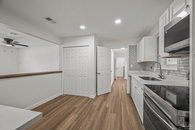 kitchen featuring white cabinets, appliances with stainless steel finishes, a sink, light wood-type flooring, and backsplash