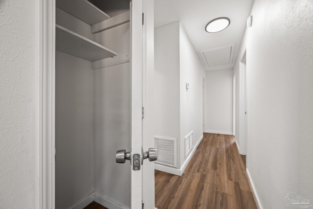 hallway with baseboards, attic access, visible vents, and wood finished floors