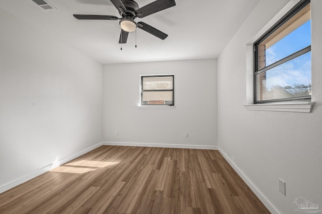 empty room featuring baseboards, wood finished floors, visible vents, and a healthy amount of sunlight