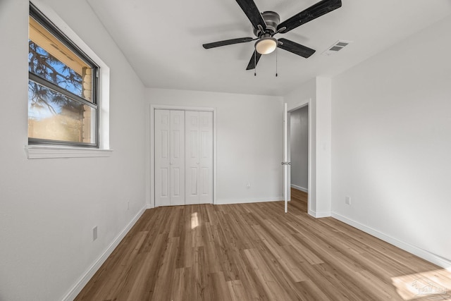 unfurnished bedroom featuring a closet, visible vents, a ceiling fan, wood finished floors, and baseboards