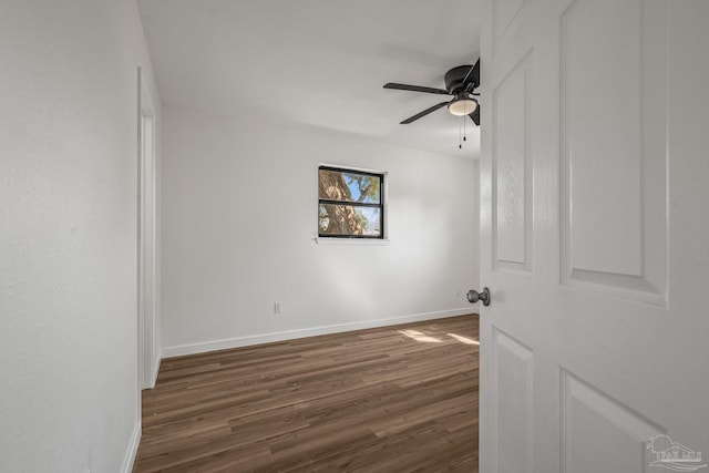 empty room with dark wood-type flooring, a ceiling fan, and baseboards