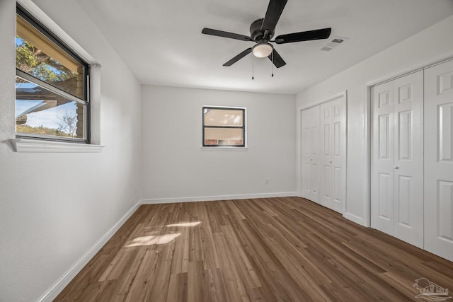 unfurnished bedroom featuring baseboards, visible vents, multiple closets, and wood finished floors