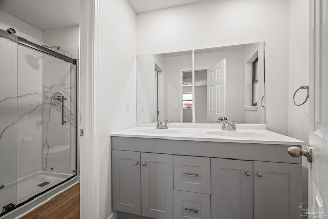 full bath with double vanity, a marble finish shower, a sink, and wood finished floors