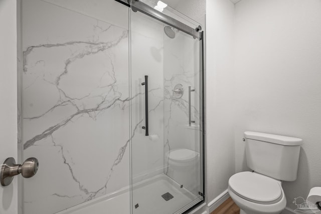 bathroom with toilet, a marble finish shower, baseboards, and wood finished floors