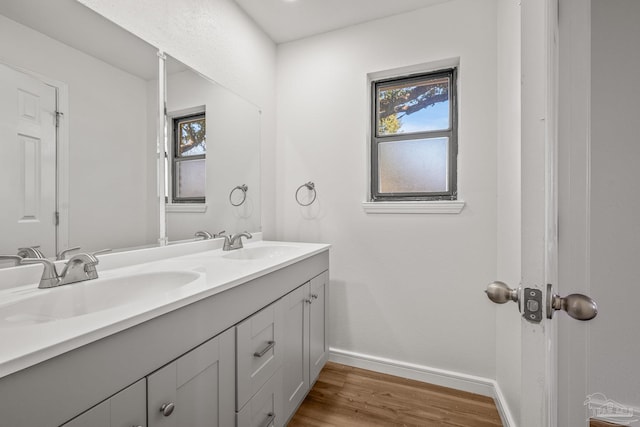 full bath with double vanity, wood finished floors, a sink, and baseboards