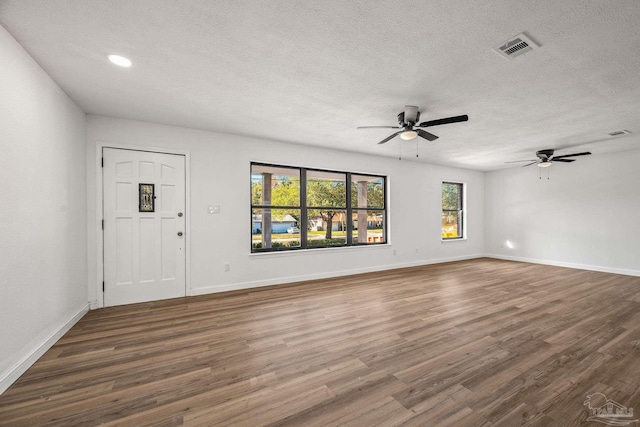 unfurnished living room featuring baseboards, a textured ceiling, visible vents, and dark wood-type flooring