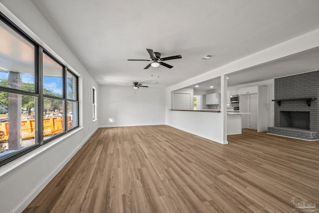 unfurnished living room featuring baseboards, visible vents, a ceiling fan, wood finished floors, and a fireplace