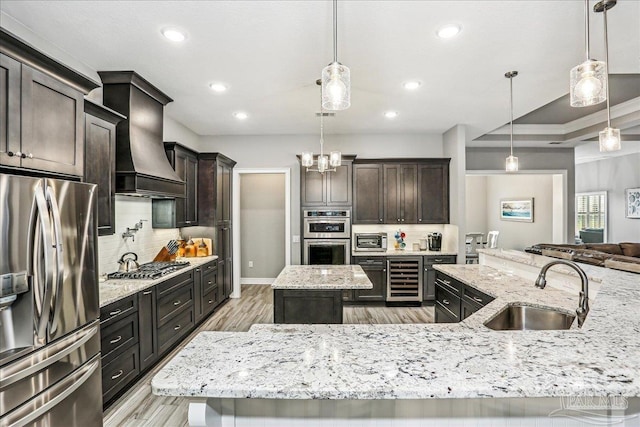 kitchen featuring a sink, a large island with sink, appliances with stainless steel finishes, custom range hood, and recessed lighting