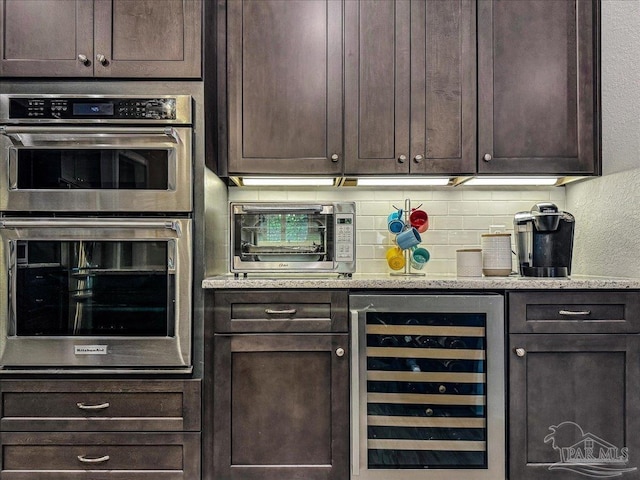 bar with stainless steel double oven, a toaster, backsplash, and beverage cooler
